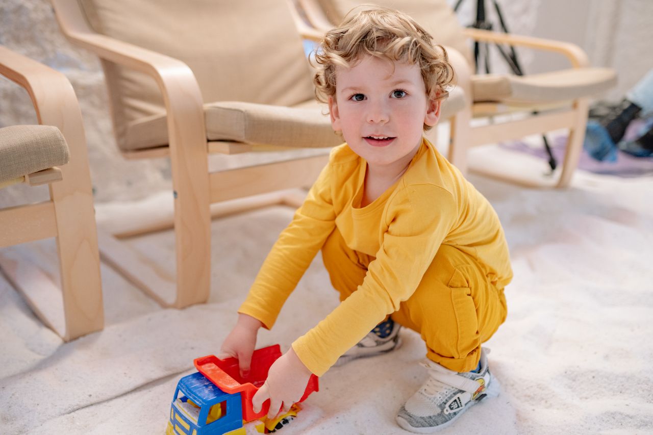 Joyful child in yellow playing with a toy truck indoors, expressing innocence and fun.